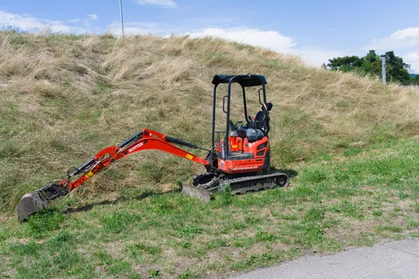 Mini excavadora roja trabajando en una ladera con pasto